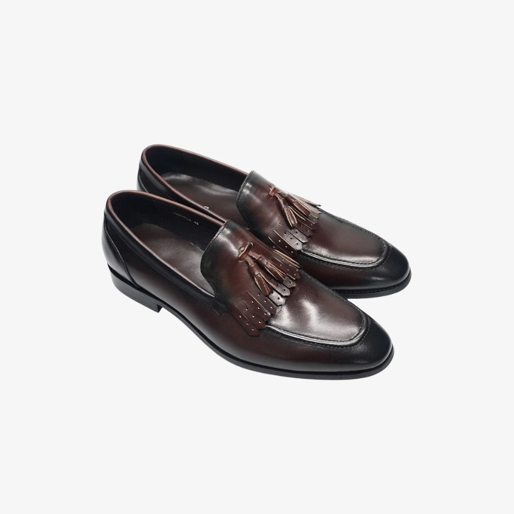 Loafers för herr i glansigt brunt läder med en elegant finish. Skorna är prydda med dekorativa tofsar och perforerade fransar på ovandelen, med en sofistikerad och tidlös stil, perfekt för formella eller professionella tillfällen.