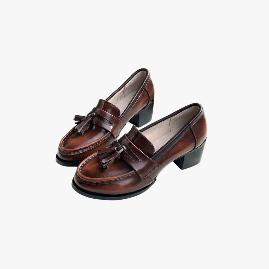 Loafers i brunt läder för dam, med dekorativa tofsar på ovansidan för en klassisk och elegant stil. Skorna har svarta fyrkantiga klackar som ger både komfort och stabilitet, perfekta för en sofistikerad look varje dag.