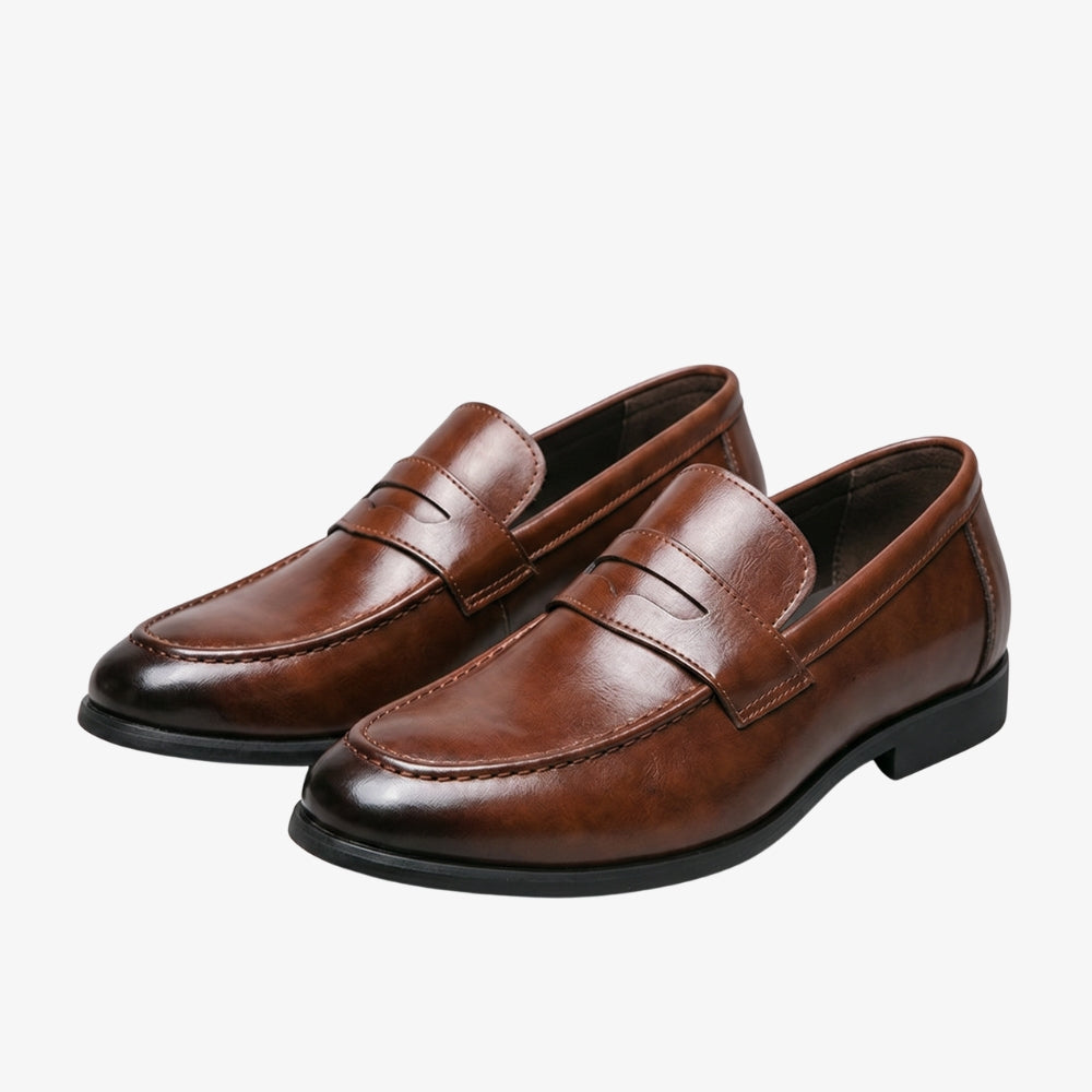 Patinerad loafer i brunt läder för herr i Penny Loafer-stil, mot en grå bakgrund