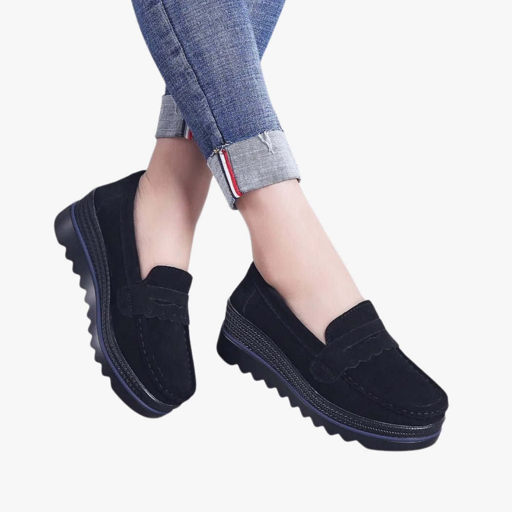 Loafers för dam i svart mocka, eleganta och bekväma, med räfflade kilsulor för bättre stabilitet. Designen har dekorativa detaljer på ovandelen och synliga sömmar, perfekt för en modern och avslappnad stil.