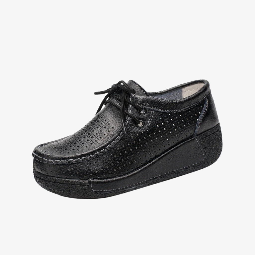 Loafers för dam i svart läder med perforerad design för bättre ventilation. De eleganta skorna har snören för exakt passform och svarta kilsulor som ger bra stöd och optimal komfort hela dagen.