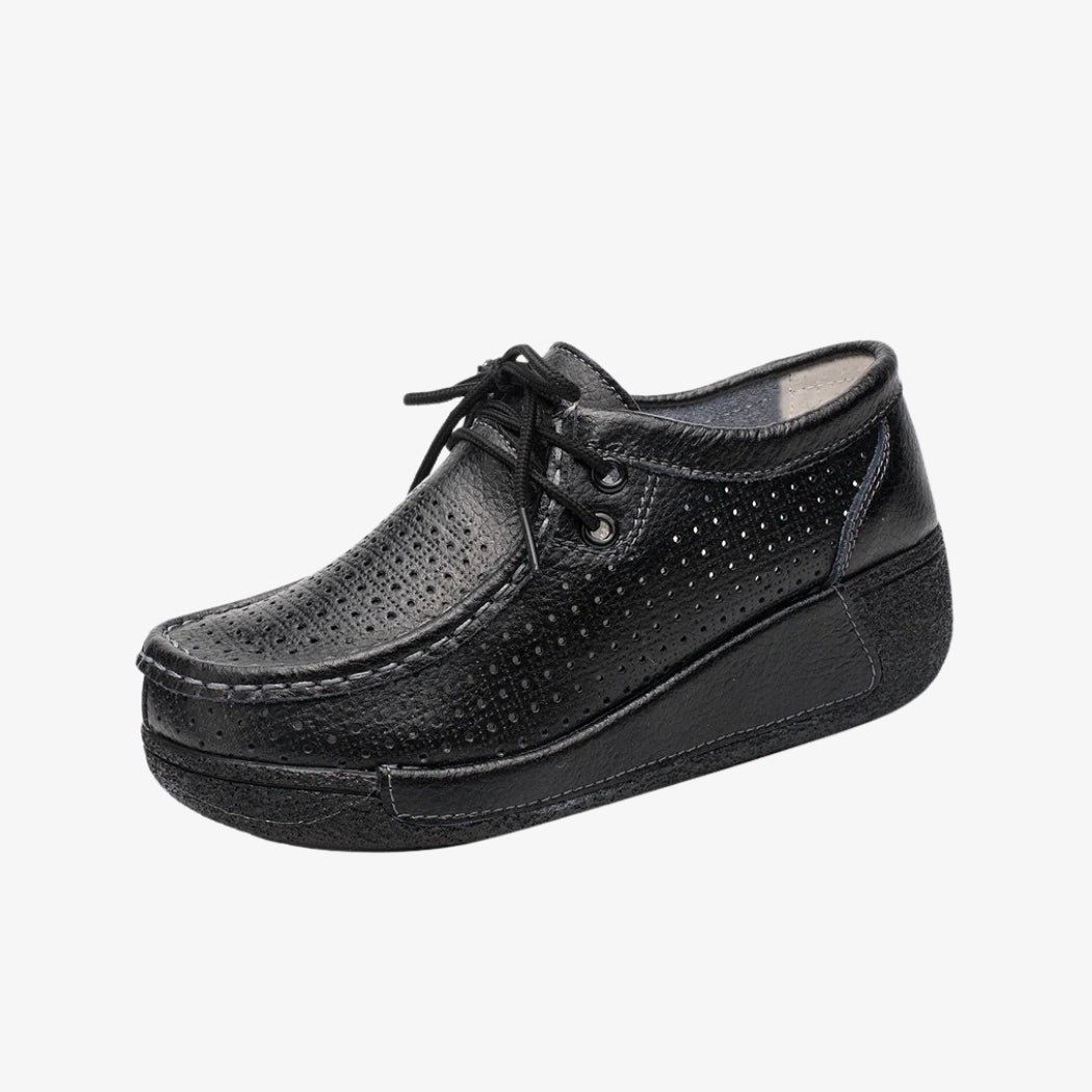 Loafers för dam i svart läder med perforerad design för bättre ventilation. De eleganta skorna har snören för exakt passform och svarta kilsulor som ger bra stöd och optimal komfort hela dagen.