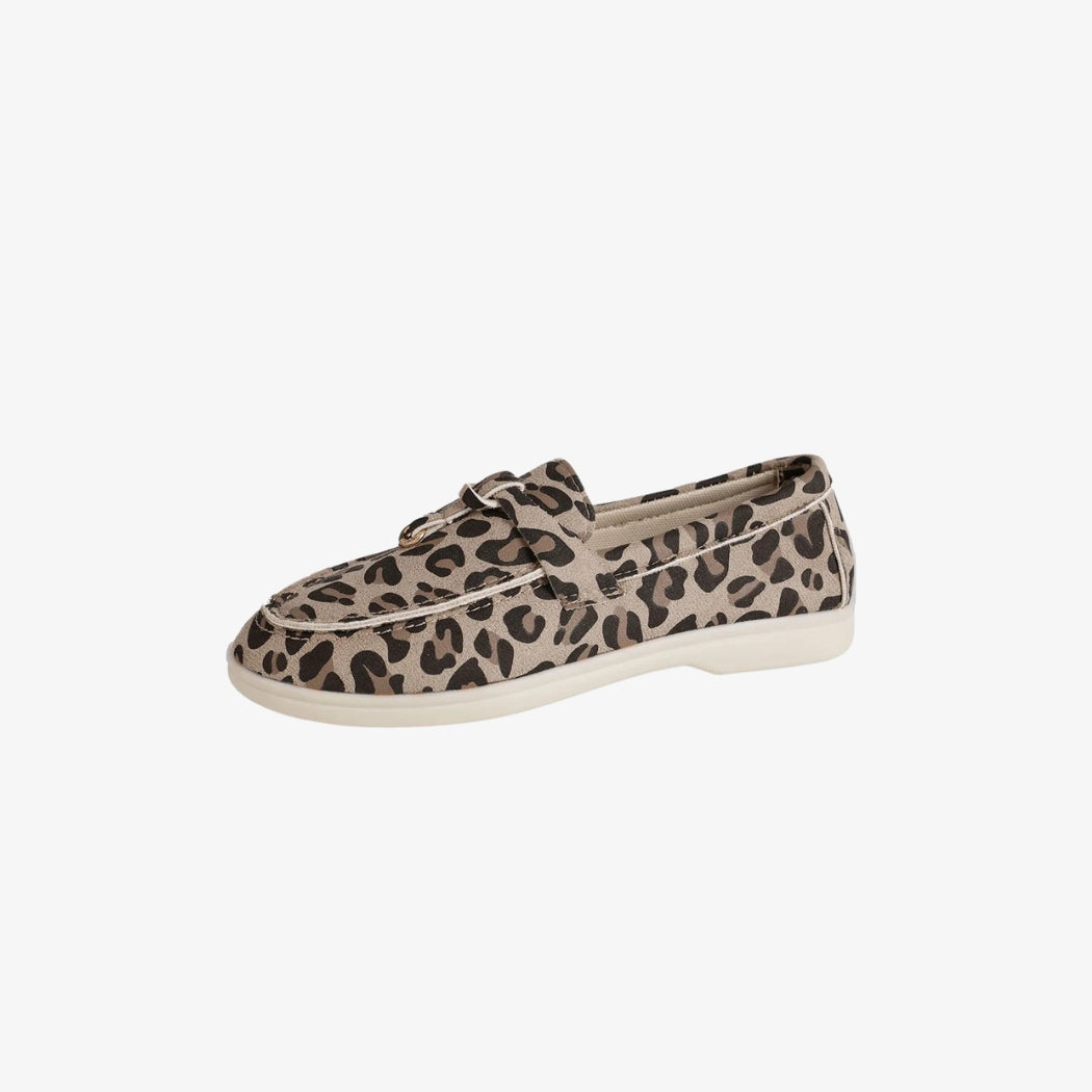 Damloafers i mocka med elegant leopardmönster. De lätta och bekväma skorna har en diskret vit sula och en dekorativ rem över foten, perfekta för en avslappnad och trendig stil.