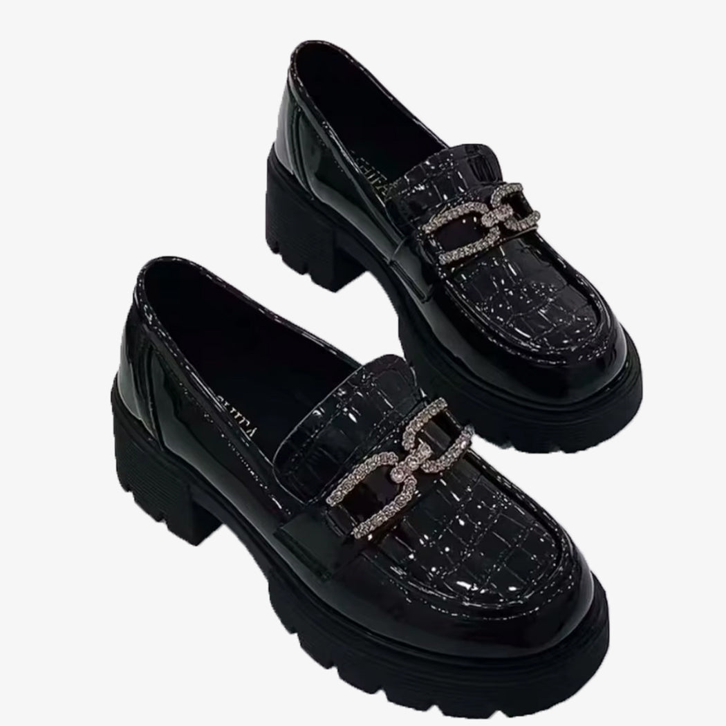 Svarta loafers med platå, lackad krokodileffekt och strass-kedja på vit bakgrund