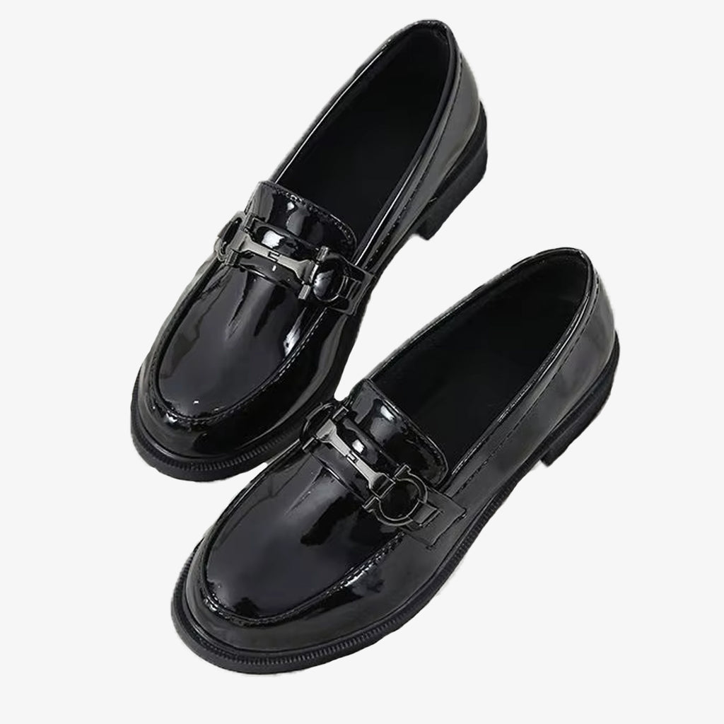Svarta patentloafers med metalldetalj på vit bakgrund
