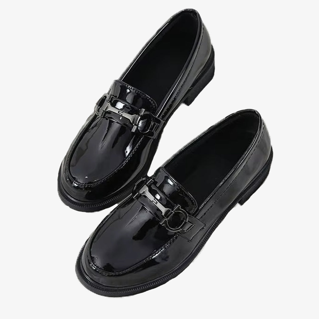 Svarta patentloafers med metalldetalj på vit bakgrund