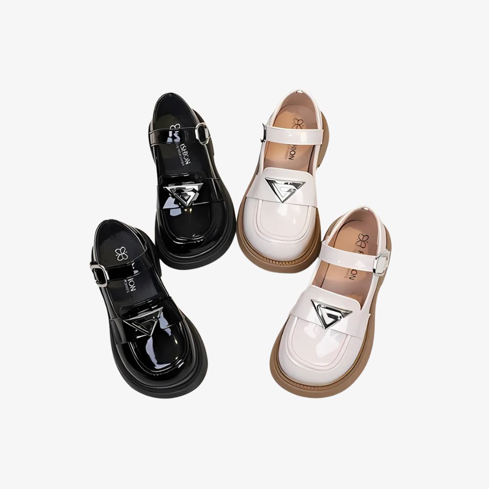 Två par blanka loafers i svart och vitt med silverfärgade detaljer, mot grå bakgrund.