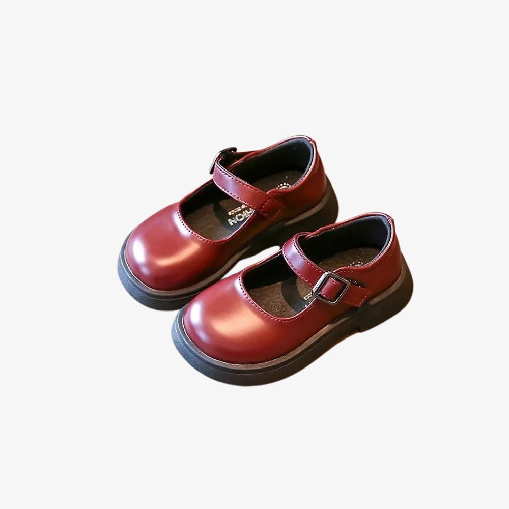 Ett par vinröda barnloafers med rem.