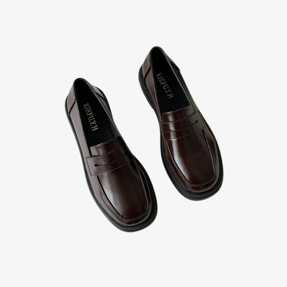 Ett par eleganta bruna loafers mot ljusgrå bakgrund.