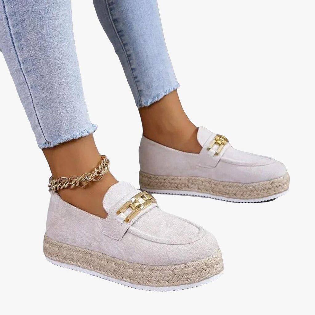 Man ser fötterna på en kvinna i jeans som bär kilsulade loafers i syntetisk mocka i beige