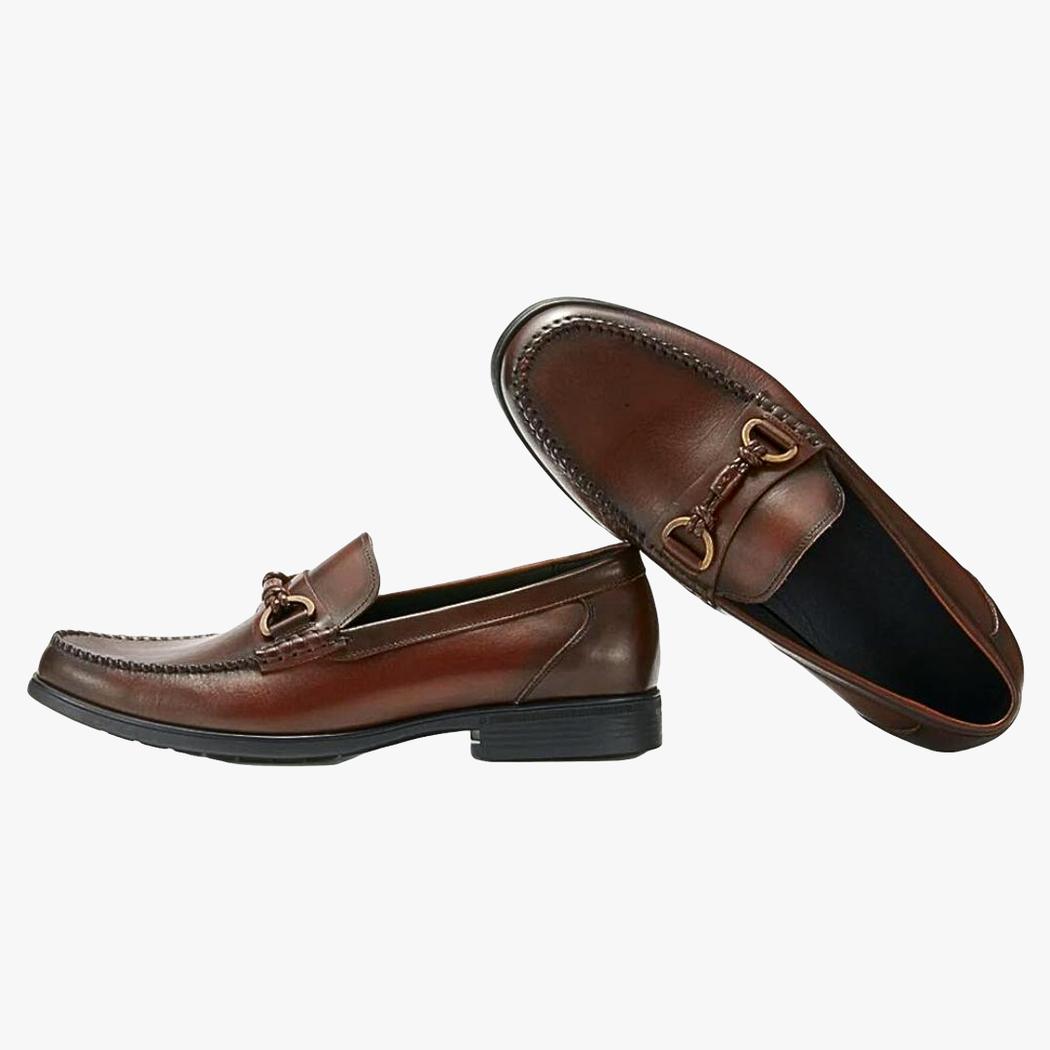 På vit bakgrund syns ett par bruna loafers i äkta läder med hästbettsbeslag för herr