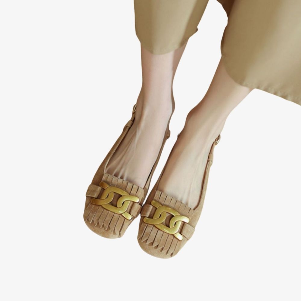 Beige loafers med fransar och guldfärgad dekor på ovansidan, burna av en kvinna
