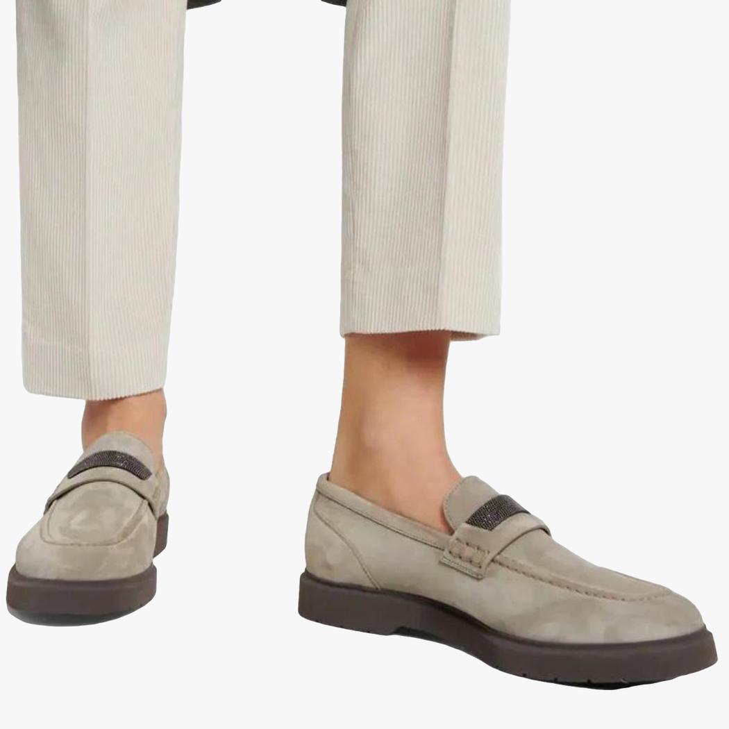 man ser fötterna på en kvinna som bär beige kostymbyxor och gråa loafers för dam i äkta mocka