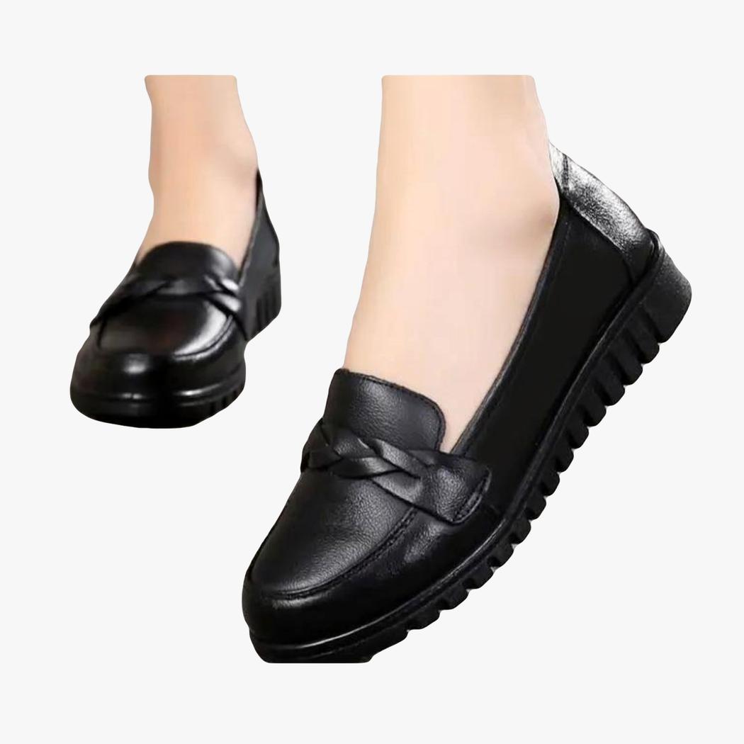 Ett par svarta loafers som bärs av en kvinna, bara fötterna syns