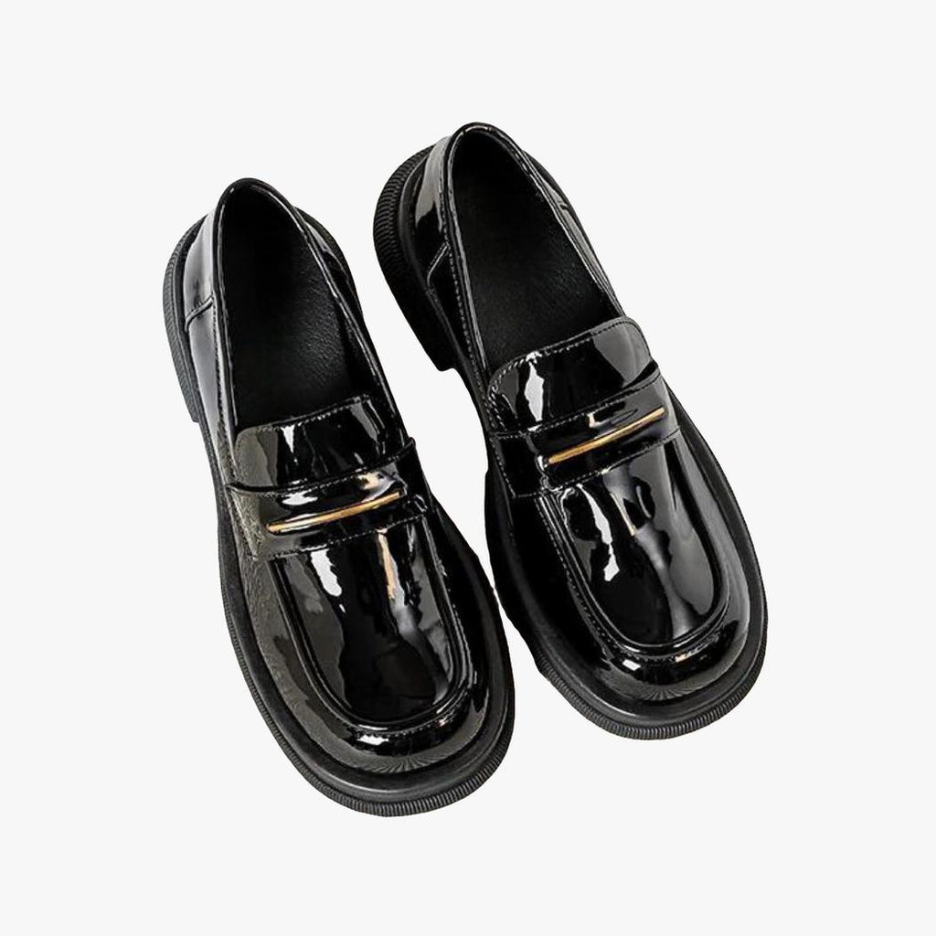 På en ljus bakgrund syns ett par svarta lackloafers i syntetiskt läder för dam