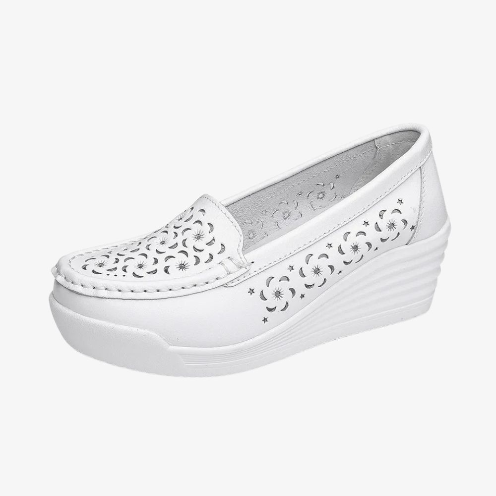 En vit loafer i profil, med kilformad sula och hål framtill och på sidorna.