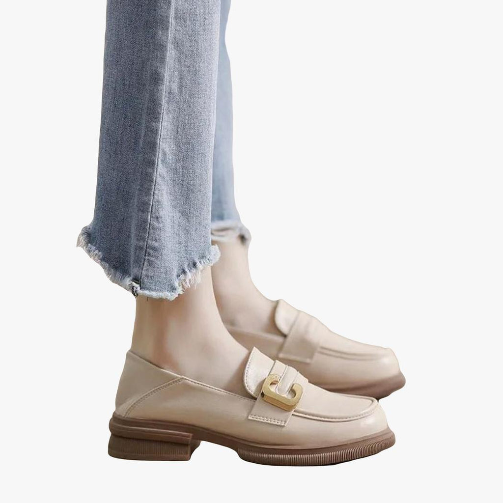 En kvinnas fötter i jeans och mjuka beige loafers i syntetläder