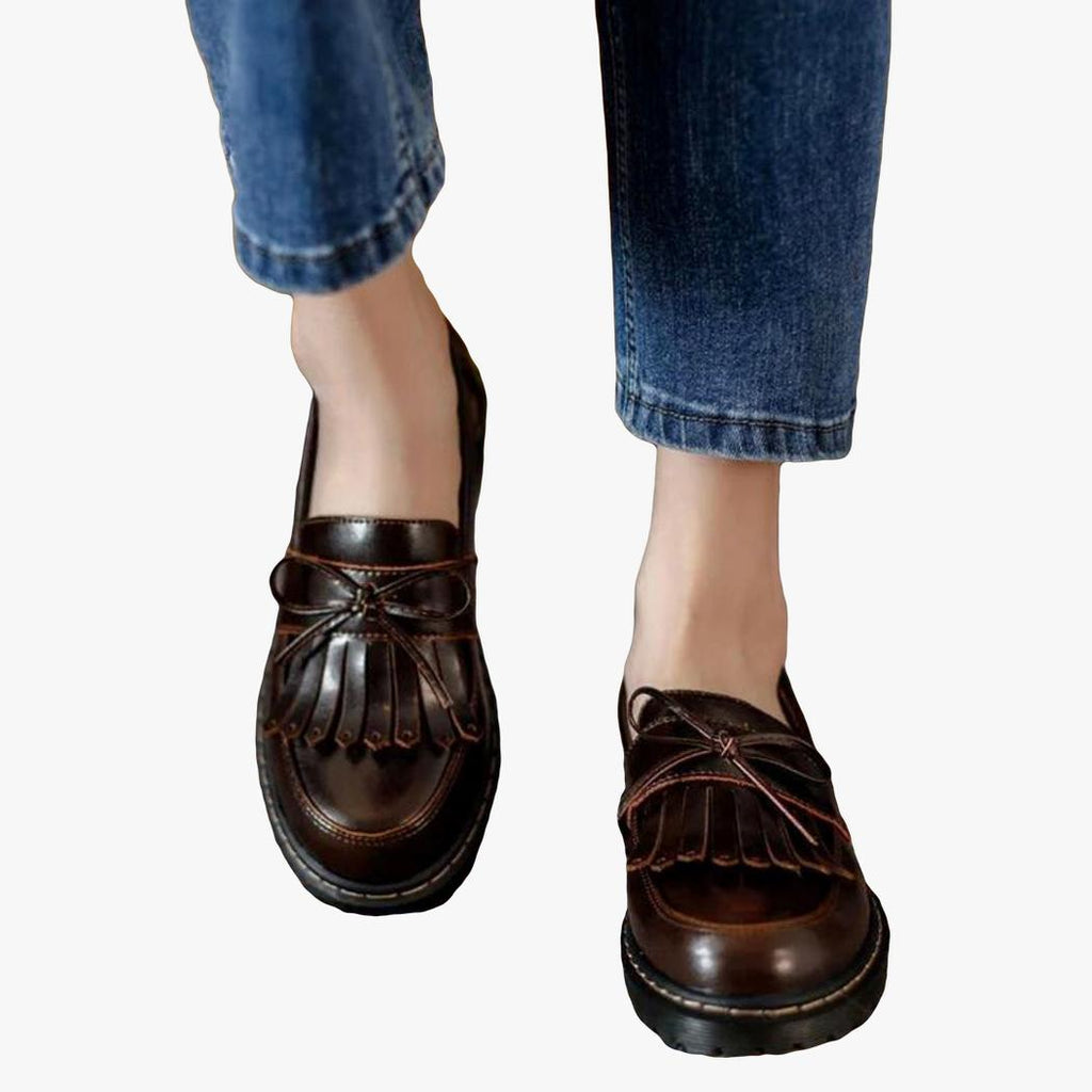 man ser fötterna på en kvinna i jeans som bär bruna loafers med fyrkantig klack och fransar i vintagestil