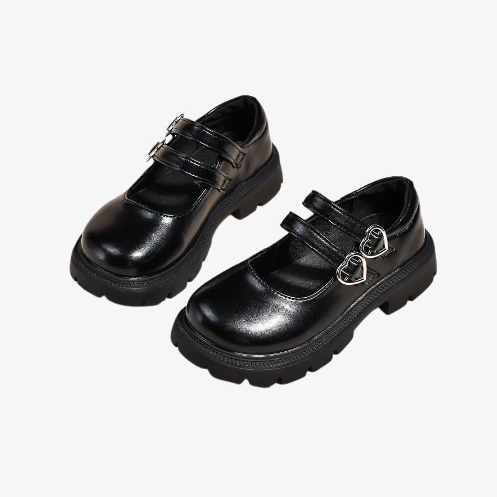Ett par svarta loafers med dubbel rem och en hjärtdetalj på ovansidan, mot grå bakgrund.