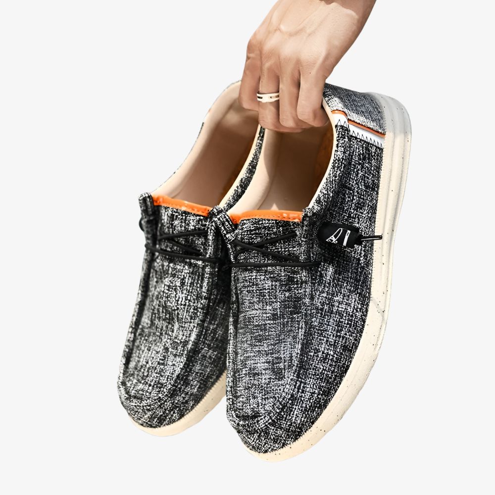 Ett par loafers för herr i grått tyg med små svarta fläckar och vit sula.