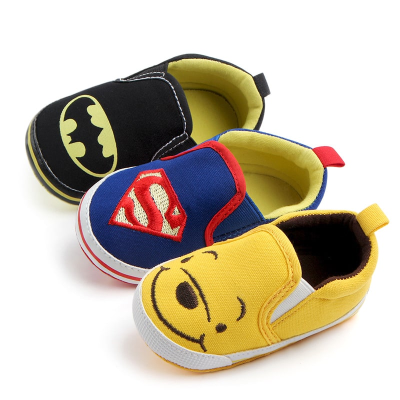 På en vit bakgrund, tre mockasiner i canvas med Batman i svart, Spiderman i blått och Nalle Puh i gult.