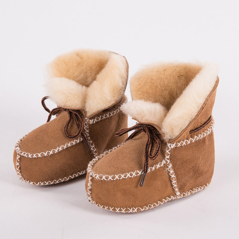 Profil: ett par indianska moccasinstövletter i kamelfärgat spaltläder med vita sömmar och beige päls på insidan. Det finns bruna snören på ovansidan