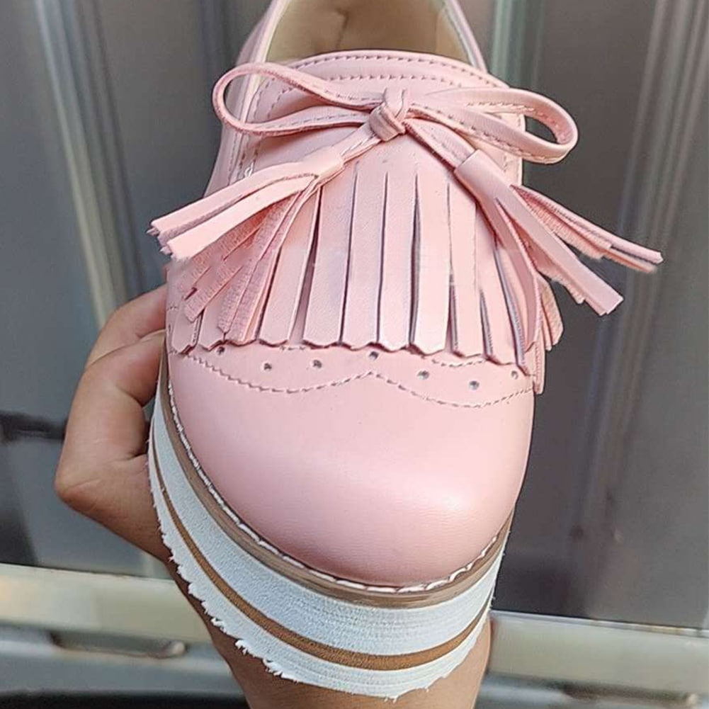 Foto av en rosa kilklädd loafer med fransar som bärs framför en dörr