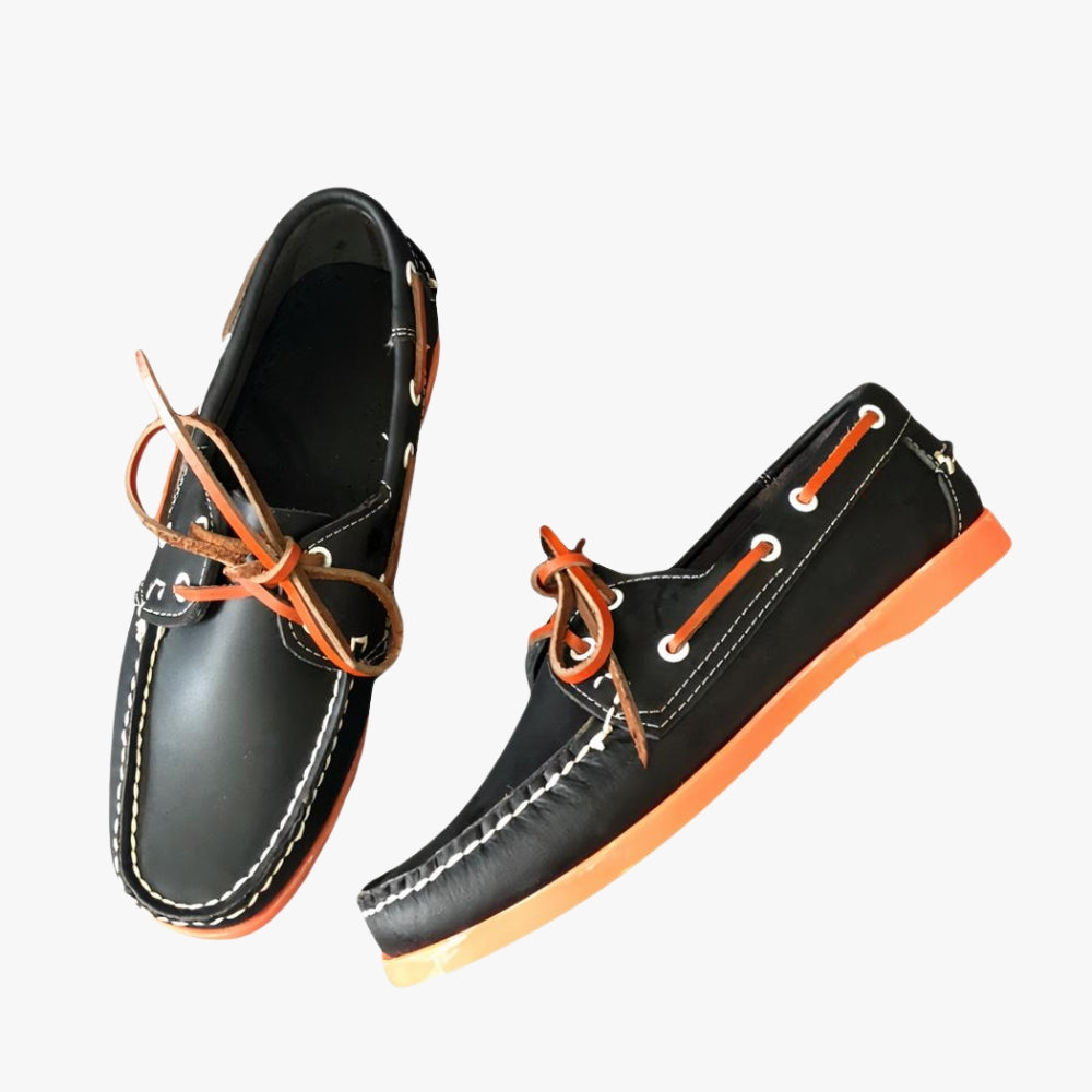 Svarta loafers med orange sula på en grå soffa