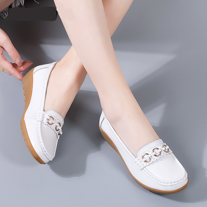 Ben av en sittande kvinna klädd i vita kilformade loafers