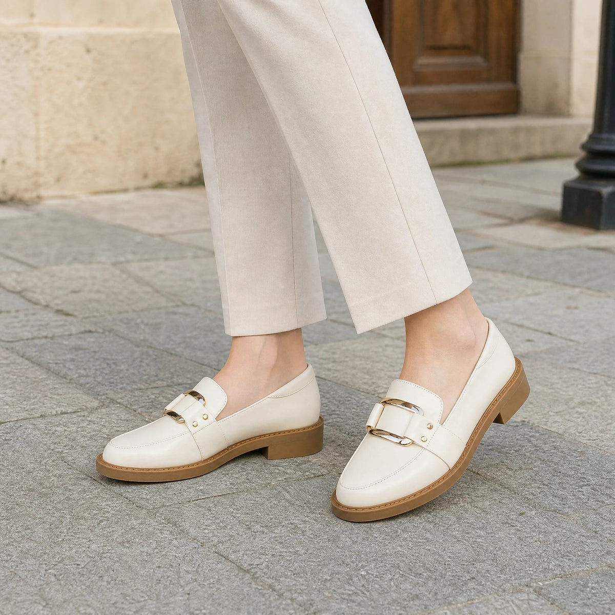 Beige loafers för dam med guldspänne och kamelfärgad sula, snett framifrån