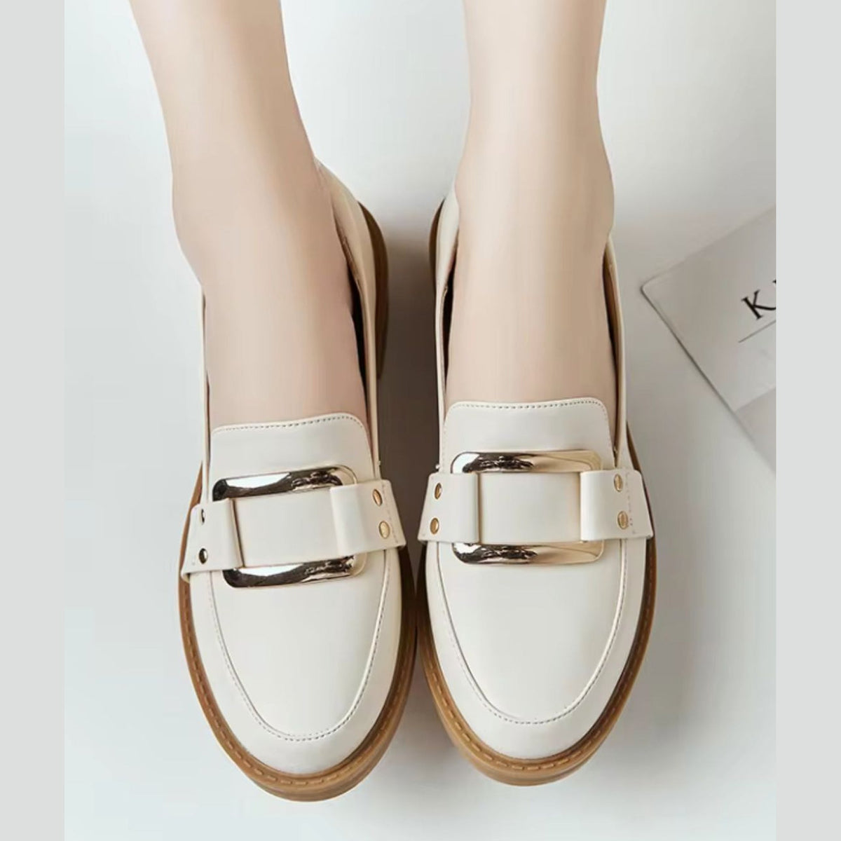 Beige loafers för dam med guldspänne och kamelfärgad sula, på foten