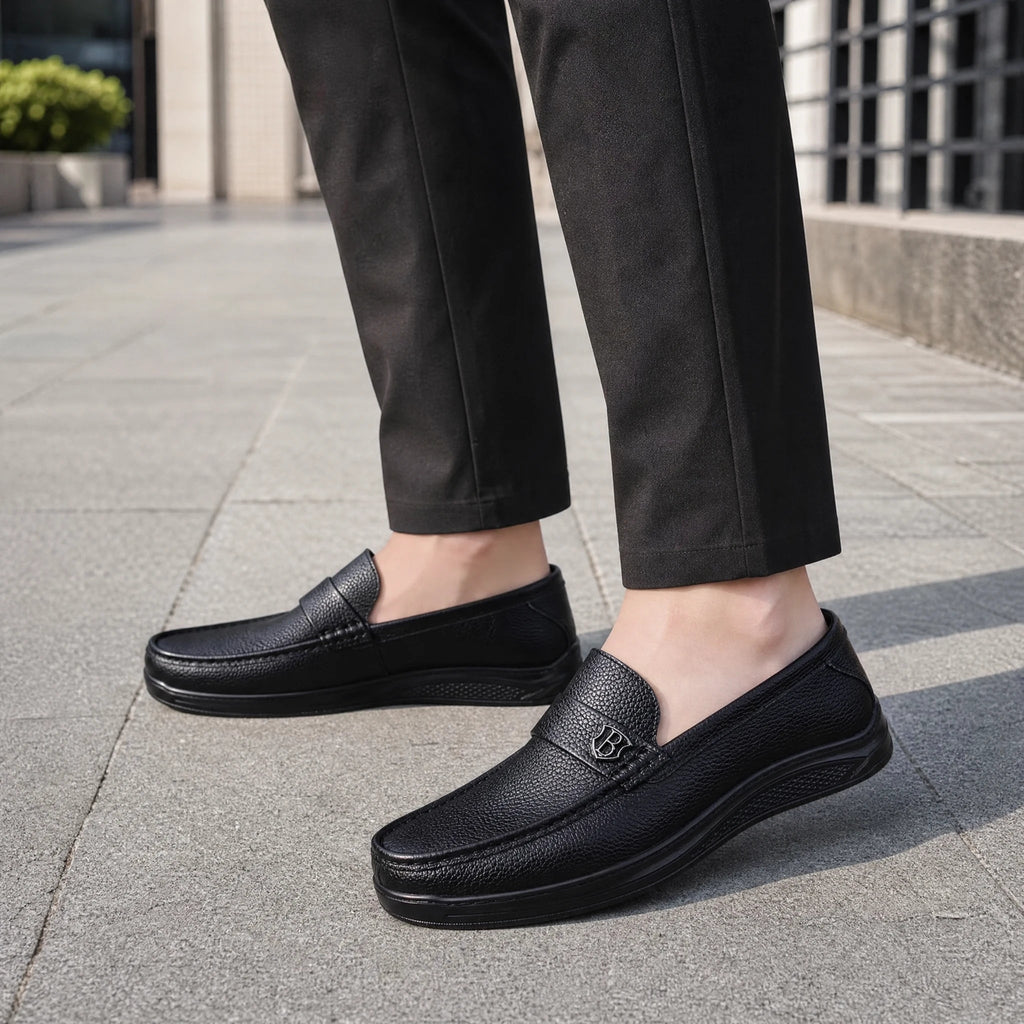 Svarta loafers för herr med tjock sula i kornigt läder, snett framifrån