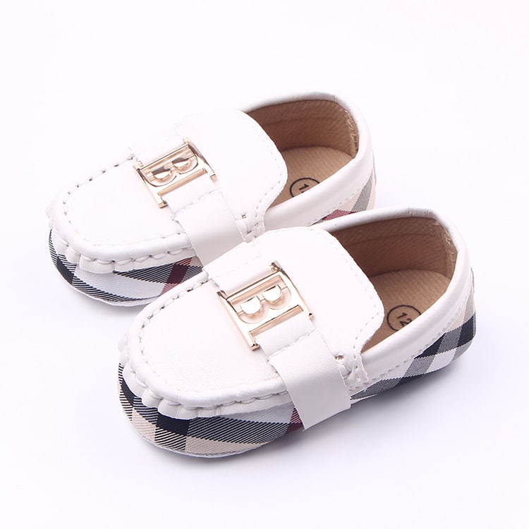 Ett par vita baby-mockasiner med burberryrutigt tyg och guldbokstaven B på ovansidan.