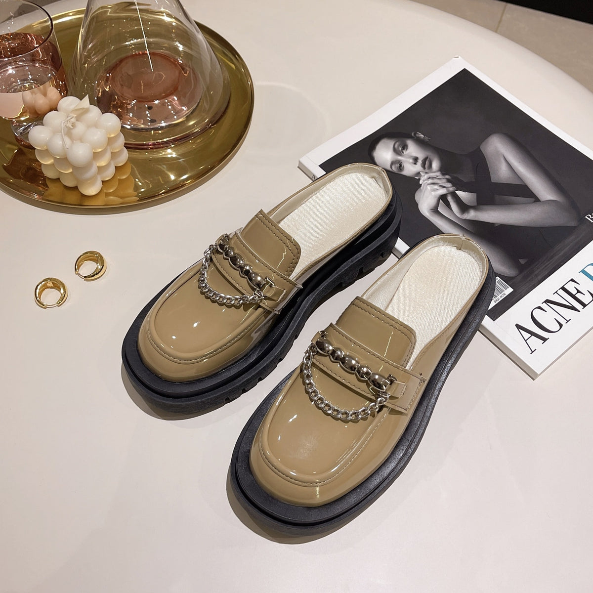 Glänsande beige loafers på ett golv med tidskrifter.