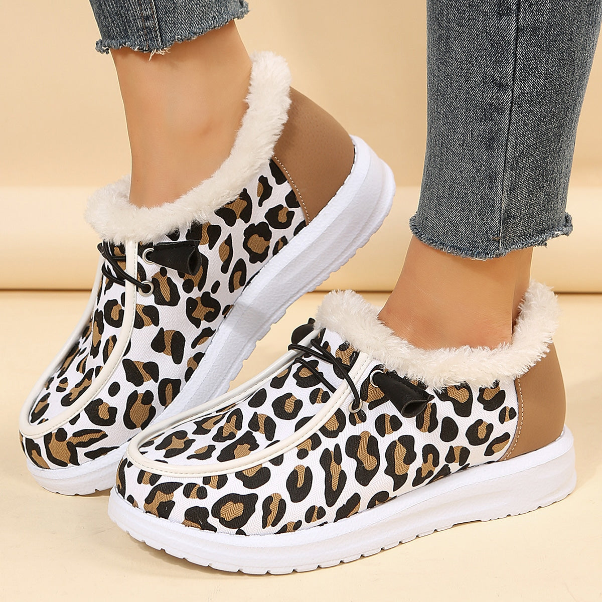 Bärs med blå jeans, ett par vita vinterloafers med leopardmönster och exponerad beige pälskant. Sulan är vit och tjock och det finns dekorativa svarta snören på toppen av skon