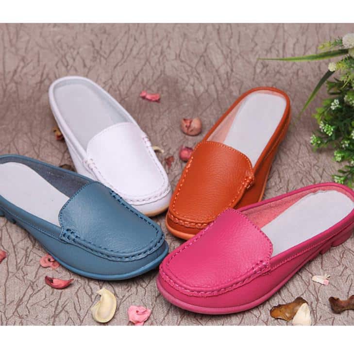 4 moccasin-mulor i blått, vitt, orange och rosa med sömmar och vita innersulor. De står på ett beige golv med rosa och beige blomblad runt om