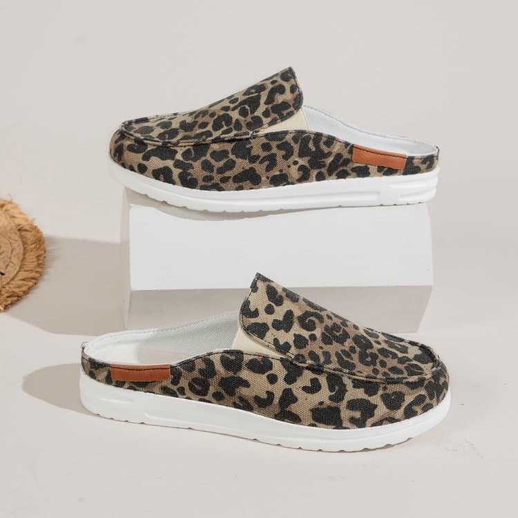 Ett par runda sportmockasiner i leopardmönstrad canvas med tjocka vita sulor visas i profil. En sko på en vit display och en undertill på ett vitt golv