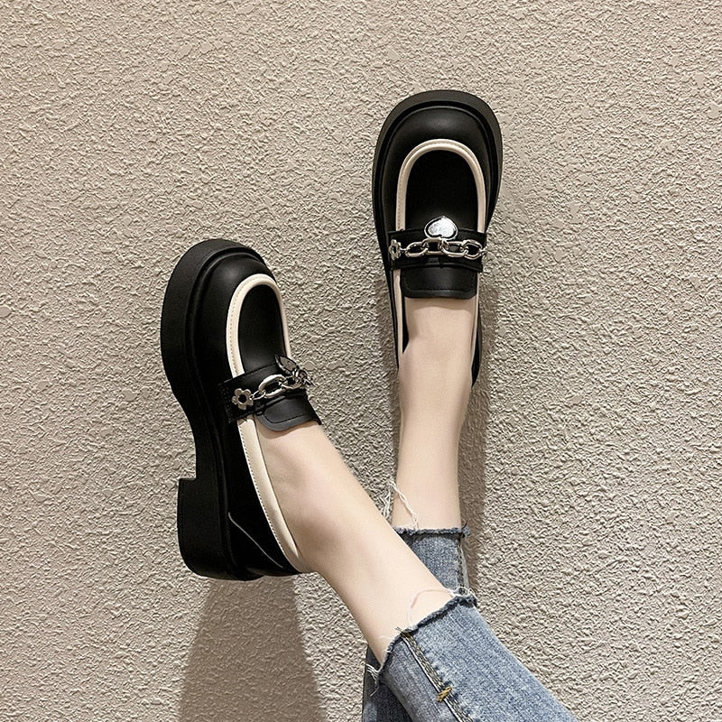 Foto av ett par svarta platåskor som bärs av en kvinna i jeans på ett beige golv