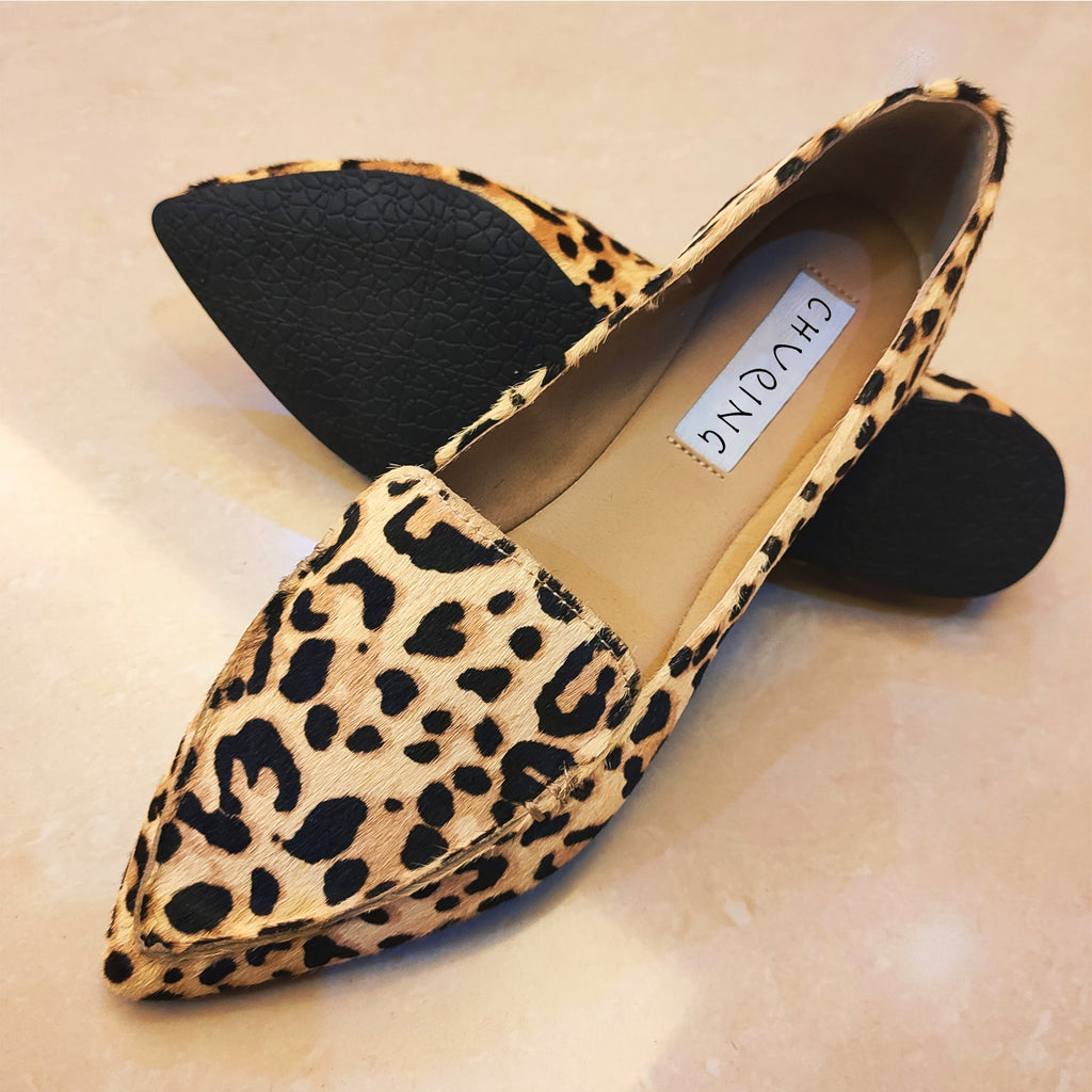 På en rosa marmorerad bakgrund, ett par spetsiga loafers i mocka och brunt leopardmönster.