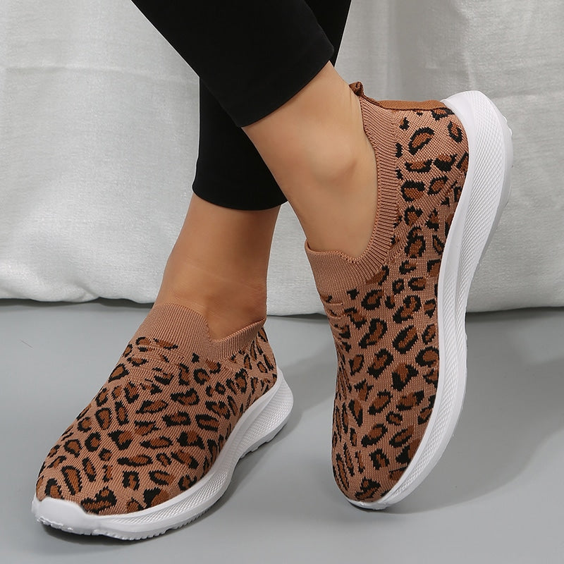 på ett grått golv, ett par stickade sportloafers med leopardmönster och tjocka vita sulor att glida runt i, som bärs nakna med svarta leggings