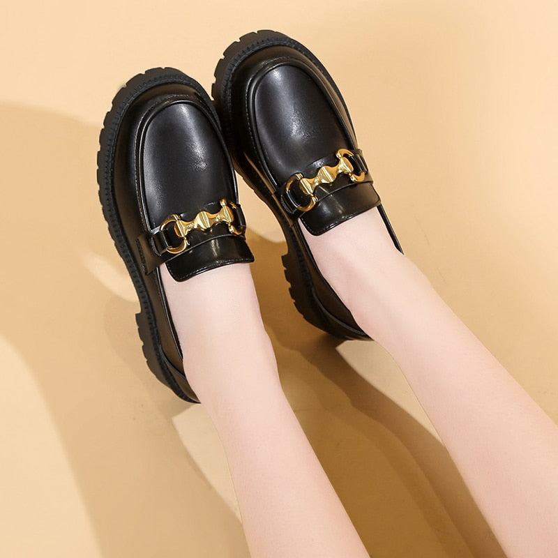 Foto av ett par svarta loafers med plattform som bärs av en kvinna mot en beige bakgrund