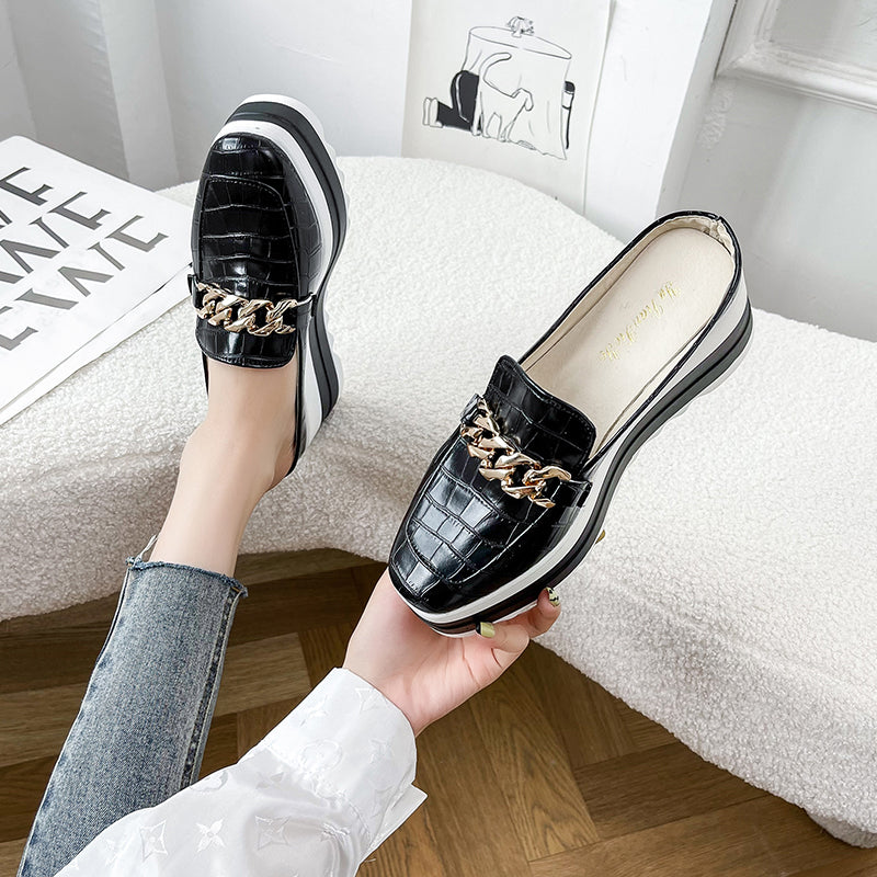 Kvinna bredvid en vit soffa som håller i en moccasin och bär en svart moccasin på vänster fot