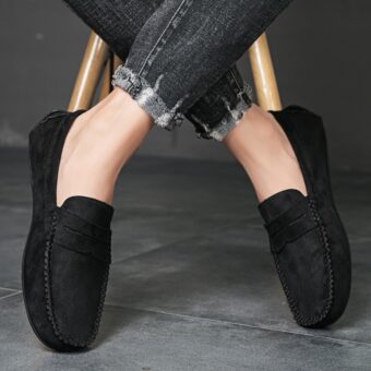 Korsade fötter i svarta loafers på ett mörkgrått klinkergolv