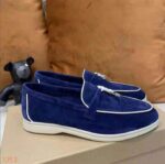 Moccasin i blå mocka med vit piping och en hård tofs på framsidan av skon som är placerad på en skokartong