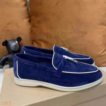 Moccasin i blå mocka med vit piping och en hård tofs på framsidan av skon som är placerad på en skokartong