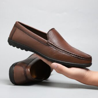 brun lädermockasin som hålls i en mans hand med det andra paret skor bakom den