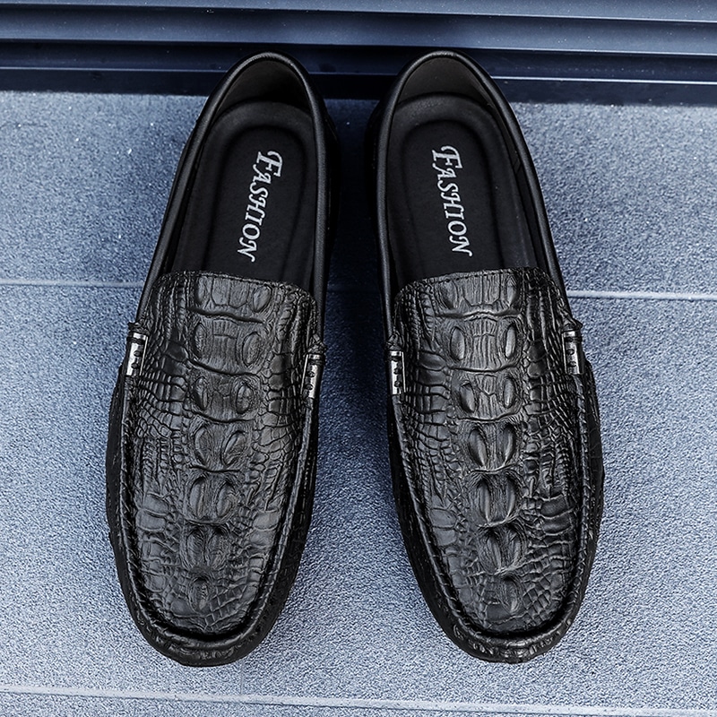 Foto av svarta läderloafers med krokodilmönster på ett grått golv