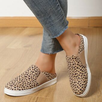 ben i jeans med synliga anklar i beige loafers med leopardmönster och vita platåskor på ett beige parkettgolv.