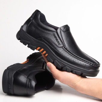Fotografi av ett par ortopediska mockaskor i svart läder med tjocka sulor. En sko ligger på golvet, den andra hålls i ena handen.