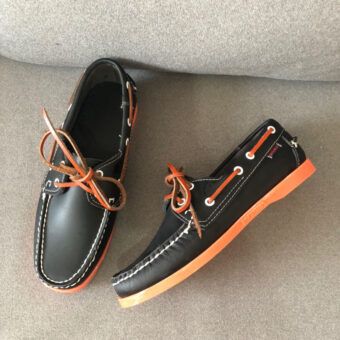 Svarta loafers med orange sula på en grå soffa